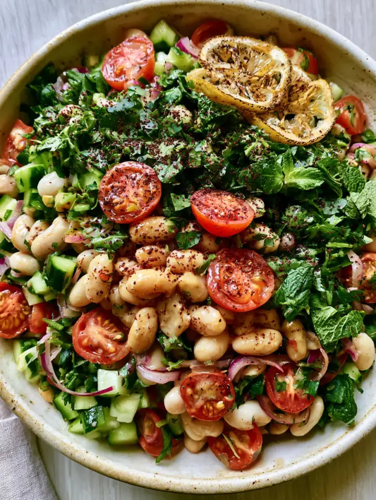 White Bean Salad with Creamy Lemon-Tahini Dressing and Charred Lemons 2 Close-up of a white bean salad with plump cannellini beans, diced cucumbers, and quartered cherry tomatoes in a glossy dressing.