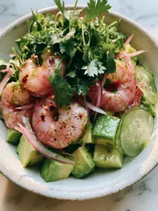 Overhead shot of chilled poached jumbo shrimp layered with avocado cubes and translucent cucumber in a rustic bowl. (shrimp avocado salad)