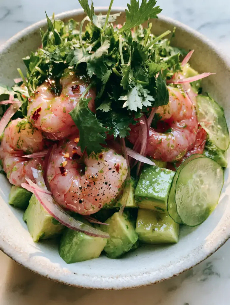 Shrimp Avocado Salad with Zesty Cilantro Lime Glaze 2 Overhead shot of chilled poached jumbo shrimp layered with avocado cubes and translucent cucumber in a rustic bowl. (shrimp avocado salad)