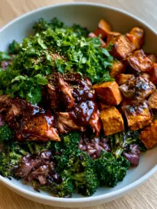 Close-up of shredded chicken coated in thick mahogany BBQ sauce with visible black pepper specks next to golden sweet potatoes. (BBQ chicken sweet potato bowl)