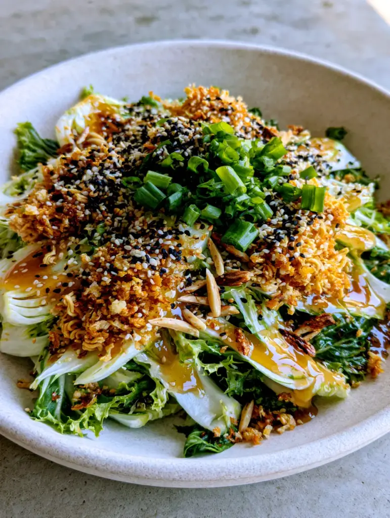 Bok Choy Salad with Toasted Ramen and Glossy Honey-Ginger Dressing 1 A shallow matte-white bowl filled with bok choy salad, garnished with black and white sesame seeds.