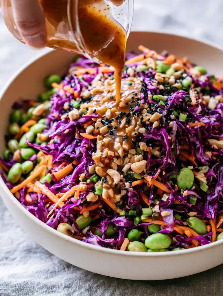Asian Crunch Salad with Velvety Peanut Dressing 1 A glossy, amber-colored peanut dressing mid-stream being poured onto a colorful Asian Crunch Salad.