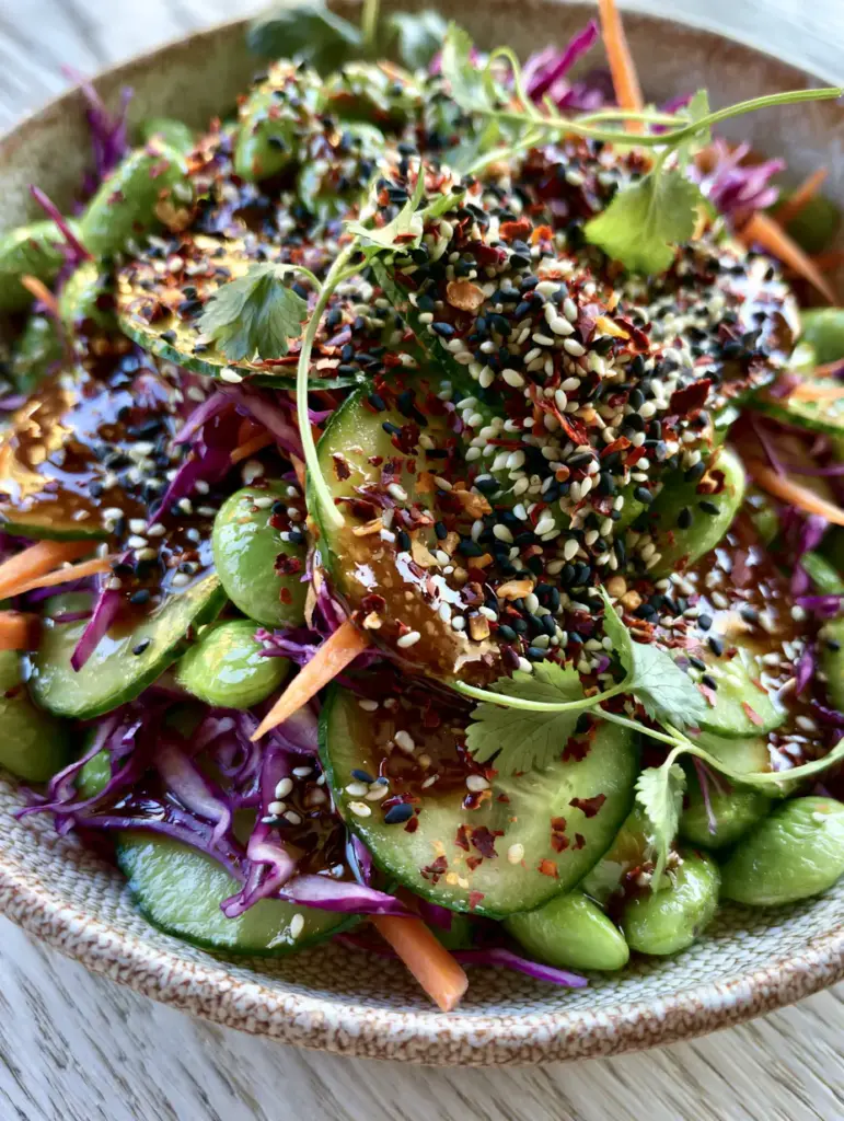 Cucumber Edamame Salad with Toasted Sesame Soy Dressing 1 Side view of a cucumber edamame salad showing shredded purple cabbage, carrots, and sesame seed garnish.