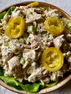 Extreme close-up of creamy Pepperoncini Chicken Salad with translucent yellow pepper rings and cracked black pepper.