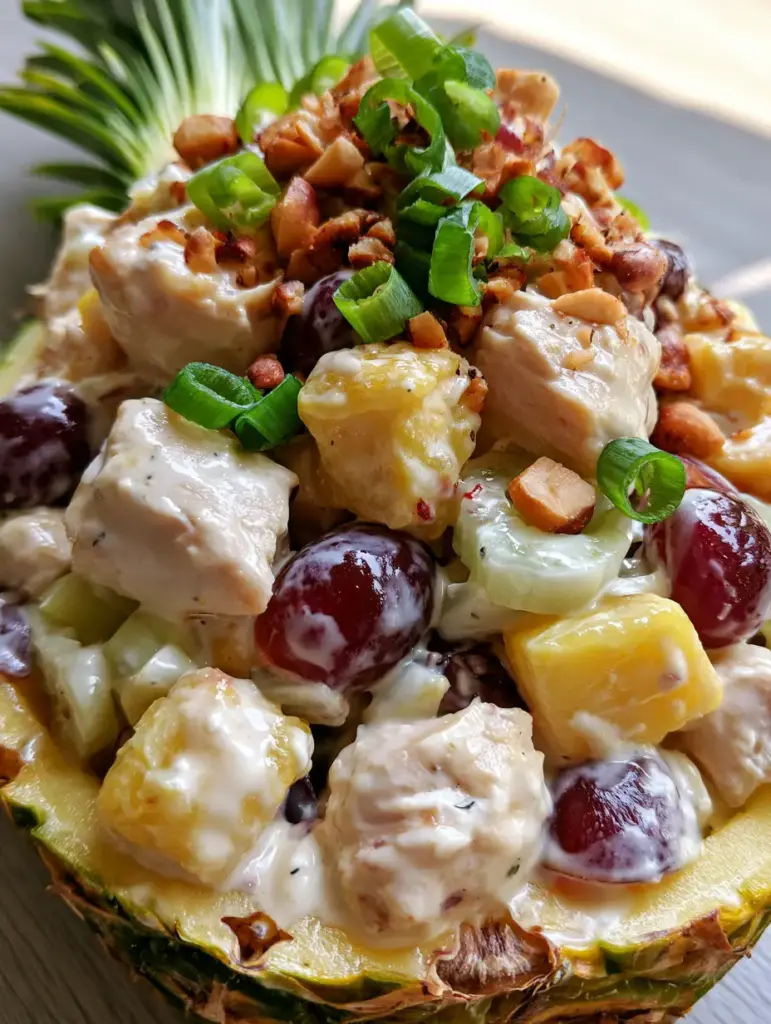 Hawaiian Chicken Salad Recipe in a Fresh Pineapple Boat 1 Top-down view of a Hawaiian chicken salad in a pineapple shell with green onion and macadamia nut garnish.