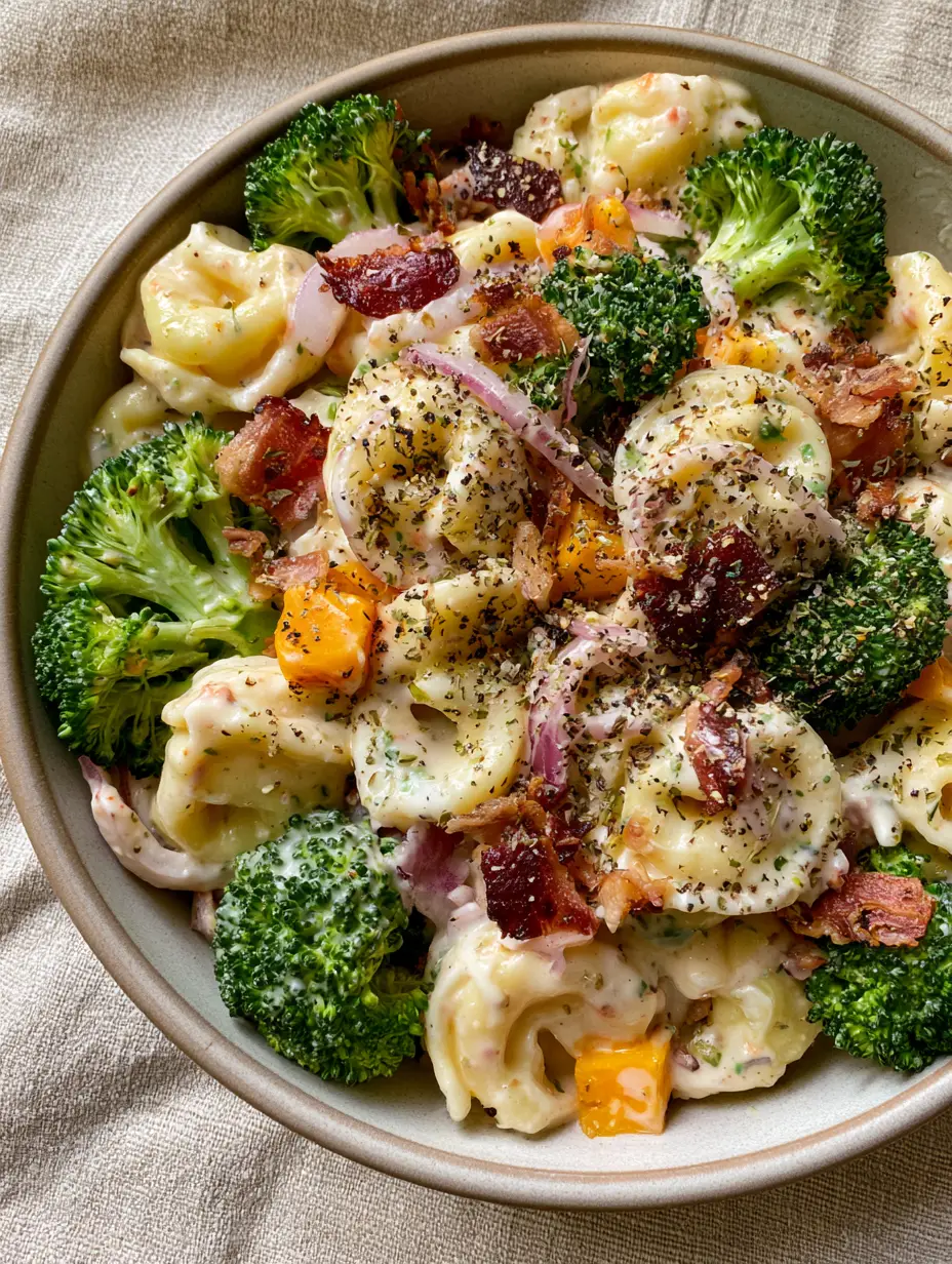 Tortellini Broccoli Salad with Crispy Bacon and Sharp Cheddar 3 High-angle smartphone photo of Tortellini Broccoli Salad in a matte stoneware bowl with soft window lighting showing thick creamy dressing and mahogany bacon.