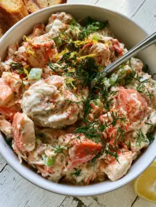 Overhead shot of creamy imitation crab salad with large pink chunks and vibrant green dill sprigs. (crab salad recipe)