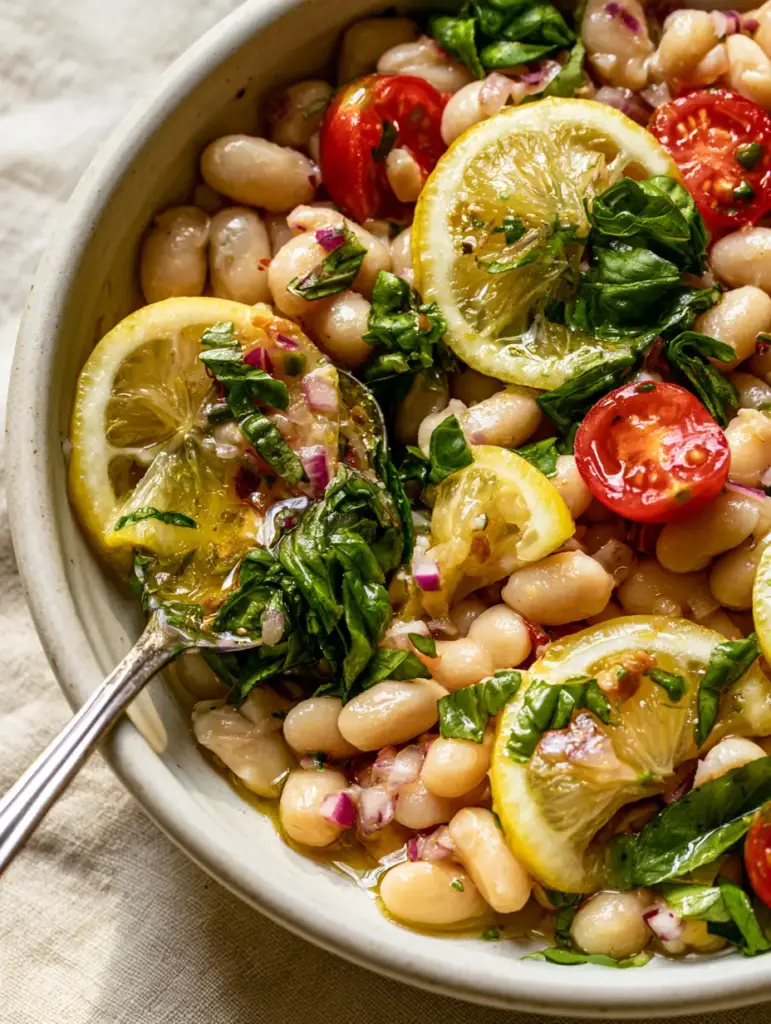 A silver spoon lifting a scoop of Lemon Basil Bean Salad, showing the wet zesty texture of the dressing.