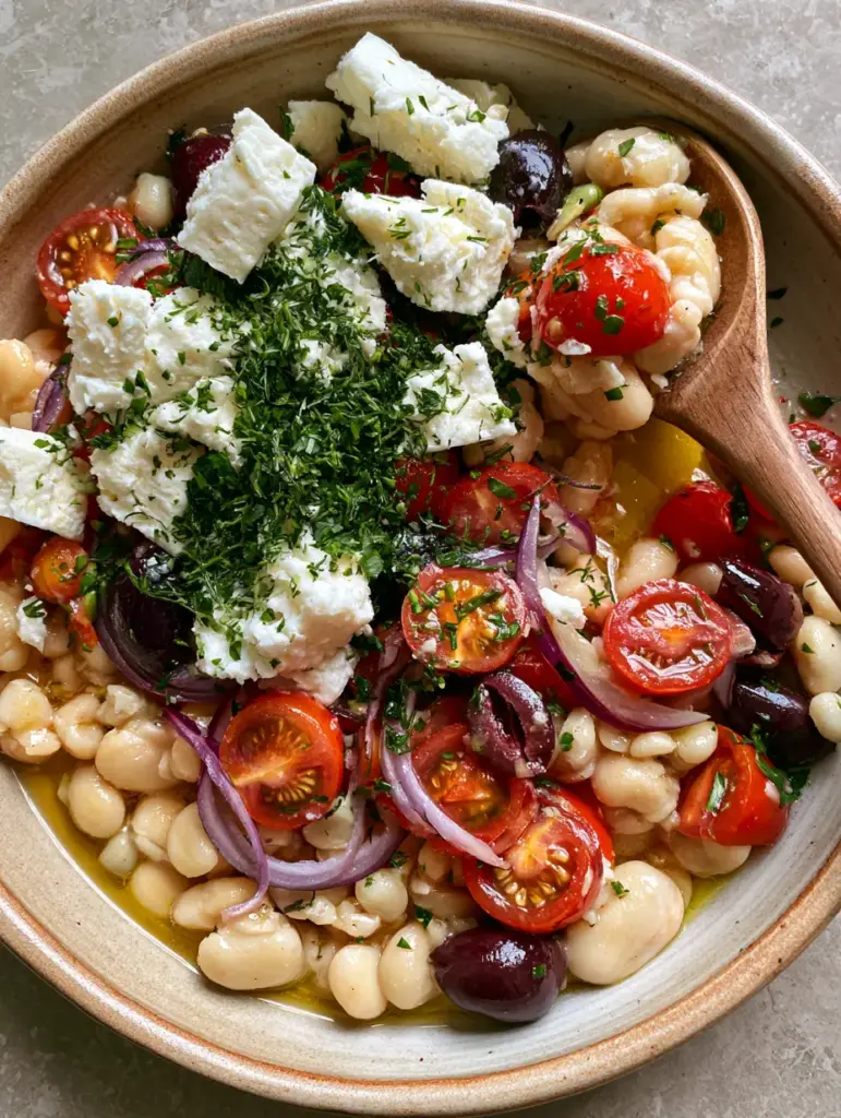 A handheld smartphone photo of a butter bean salad showing textures of feta, olives, and ruby-red tomatoes.