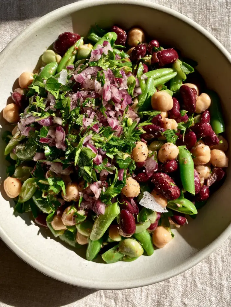 Three-Bean Salad with Crisp Green Beans and Zesty Vinaigrette 1 Close-up of three-bean salad in a matte white ceramic bowl featuring finely diced red onion and cracked black pepper.