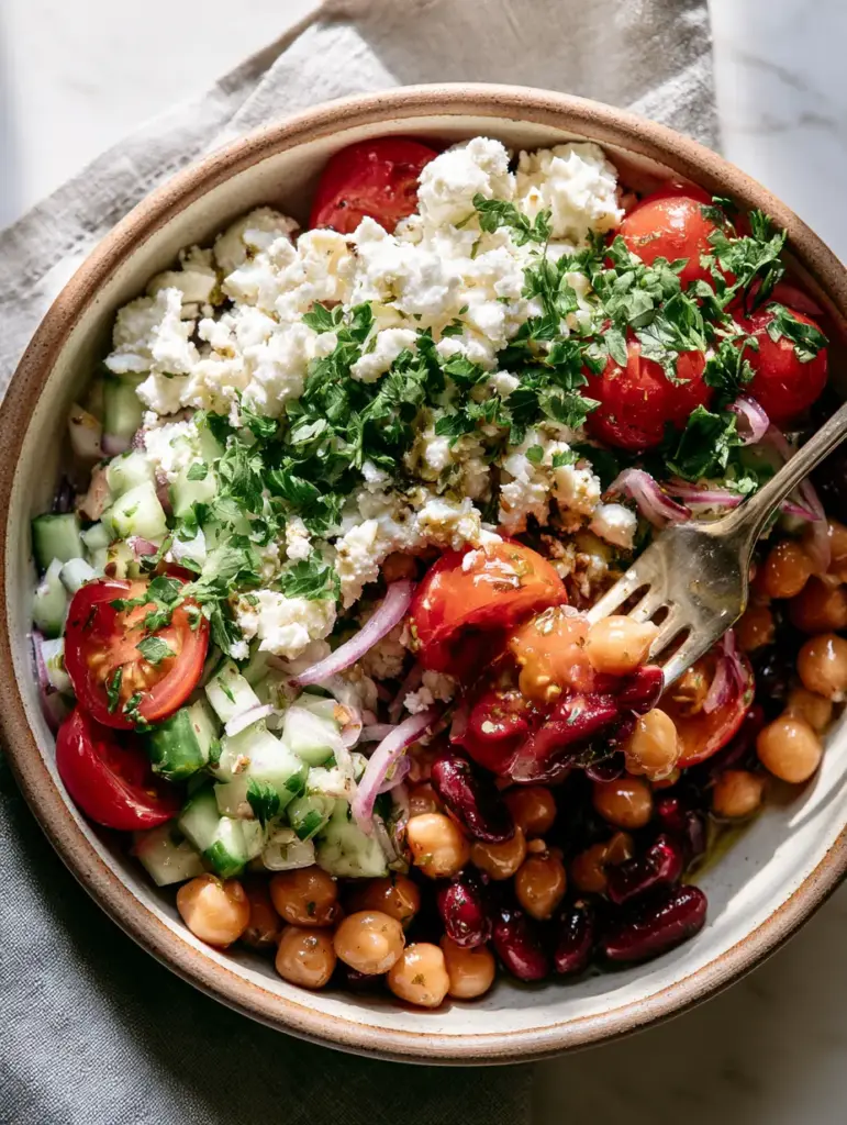 Close up of glossy lemon vinaigrette coating a protein-packed bean salad with crumbled feta cheese.