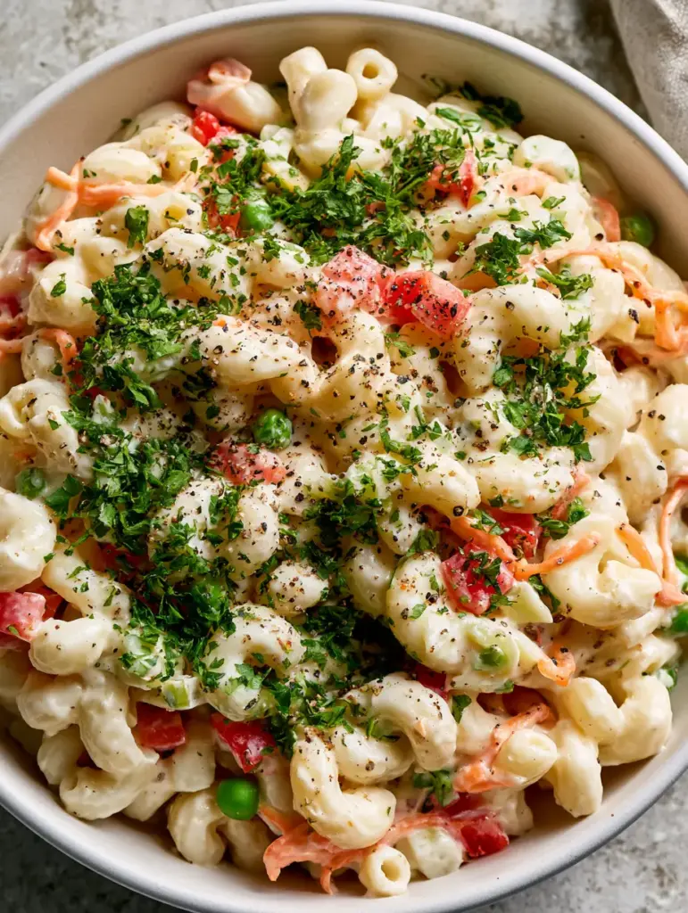 A vibrant ceramic bowl filled with macaroni salad, shredded carrots, and fresh parsley. (healthy macaroni pasta salad)